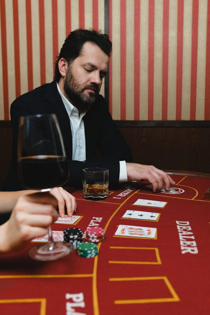 pexels photo 6664186 A man concentrating on a poker game at a casino table with cards, chips, and drinks.